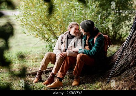 Portrait of young couple relaxing by tree while enjoying hike in forest Stock Photo