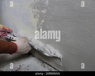 finishing puttying the wall with a wide spatula in the hands of the plasterer, leading the trowel from the bottom up along the wall surface Stock Photo