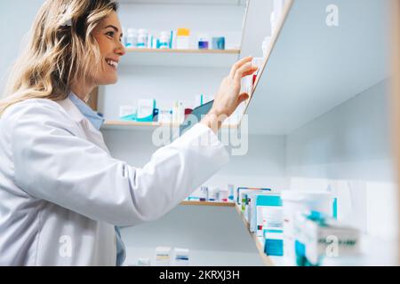 Female doctor getting medication from a shelf in her pharmacy. Female healthcare worker dispensing prescription medication. Woman working in a chemist Stock Photo