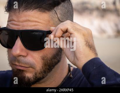 Hipster man with hands on chin on the beach. Worried attitude. Stock Photo