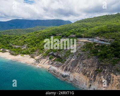 Aerial view of tropical road alongside beautiful blue water and sandy beach. Stock Photo