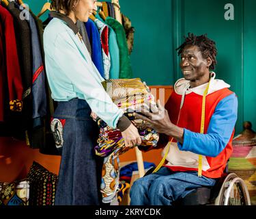 two tailors in their shop workshop passing fabrics to create clothes, example of small business and inclusion of people with disabilities Stock Photo