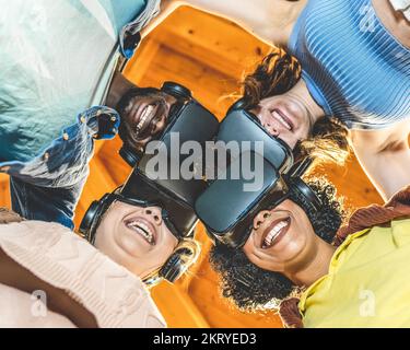 Portrait from below of a team of online players with augmented reality headset, four people of mixed ethnicity and different age embracing before the Stock Photo