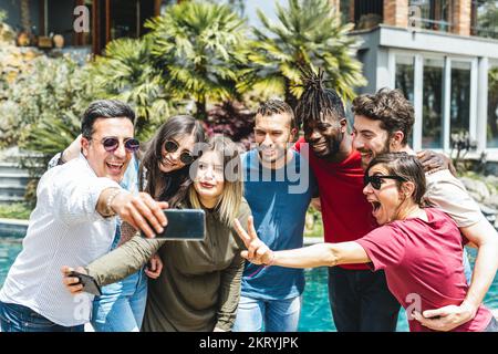 Group of mixed age range friends taking selfy in the garden of the villa with pool on holiday, people having fun on vacation, diversity and happiness Stock Photo