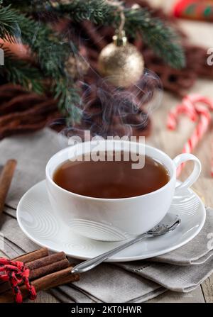 Cup of steaming hot tea on a wooden table with Christmas decorations in background Stock Photo