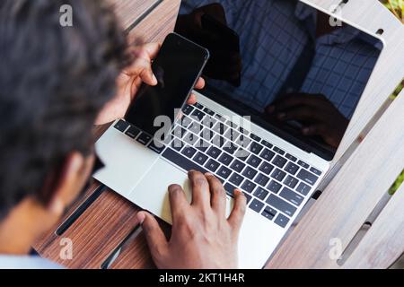 man person working with laptop computer and reading message from modern smart phone Stock Photo