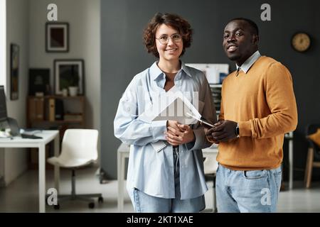 Portrait of two colleagues smiling at camera while working together at IT office Stock Photo
