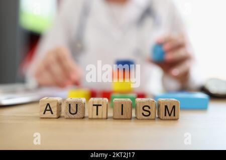 Word autism assembled from wooden blocks close-up and psychiatrist doctor with colored blocks. Stock Photo