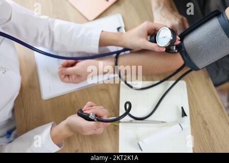 Female doctor using sphygmomanometer checks patient's blood pressure in medical clinic. Stock Photo
