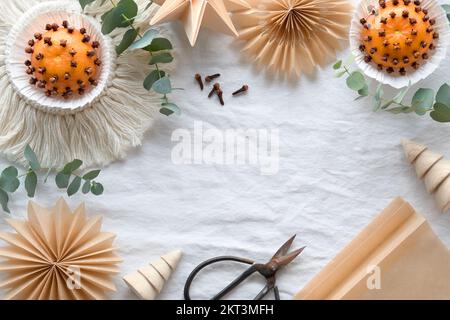 Fragrant pomander balls handmade from tangerines and cloves. Handmade paper stars from brown baking paper. Flat lay on off white textile tablecloth Stock Photo