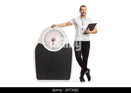 Sports coach holding a clipboard and standing next to a weigh scale isolated on white background Stock Photo