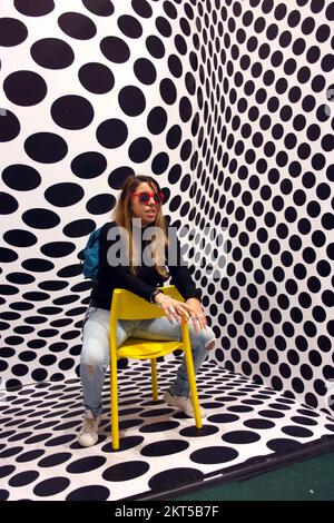 young protagonist posing on yellow chair and black and white psychedelic background in a modern room Stock Photo