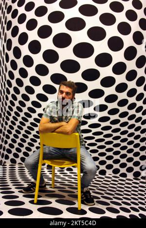 young protagonist posing on yellow chair and black and white psychedelic background in a modern room Stock Photo