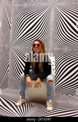 young protagonist posing on yellow chair and black and white psychedelic background in a modern room Stock Photo