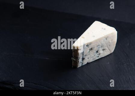 Blue cheese, dor blue or roquefort mold cheese slice on cutting board with basil leaves, lifestyle food. Stock Photo