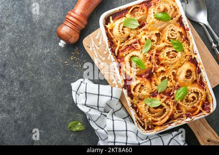 Lasagna. Homemade lasagna pasta rotolo bake with tomato sauce, cream cheese and basil on white skillet on dark slate, stone or concrete background. It Stock Photo