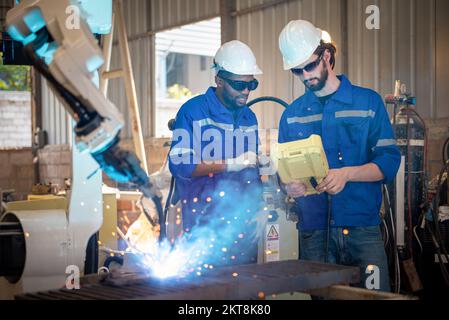 Two engineers mechanic using computer controller Robotic arm for welding steel in steel factory workshop. Industry robot programming software for auto Stock Photo