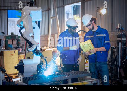 Two engineers mechanic using computer controller Robotic arm for welding steel in steel factory workshop. Industry robot programming software for auto Stock Photo