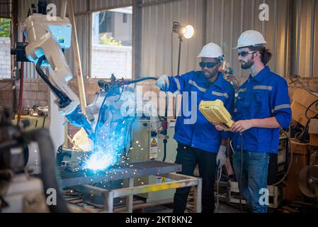 Two engineers mechanic using computer controller Robotic arm for welding steel in steel factory workshop. Industry robot programming software for auto Stock Photo