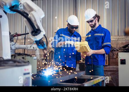 Two engineers mechanic using computer controller Robotic arm for welding steel in steel factory workshop. Industry robot programming software for auto Stock Photo