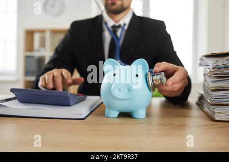 Male financial advisor or accountant inspects and listens to piggy bank with stethoscope. Stock Photo