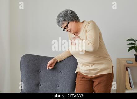 Senior woman at home experiences severe chest pain that may be symptom of heart attack. Stock Photo