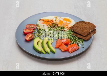 Fried eggs with avocado, tomato, salmon and micro green sprouts Stock Photo