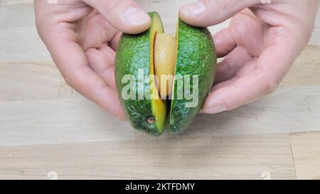 Young man cutting avocado top view on wooden cutting board. Perfectly ripe  avocado in hands, making toasts in modern white kitchen. Healthy eating and  Home cooking concept. photo – Food Image on