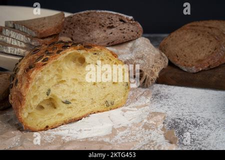 Different types of sliced bread and a loaf on a wooden background . Spilled flour. Front view. Copy space. A half cut loaf . Fresh crusty bread. Stock Photo
