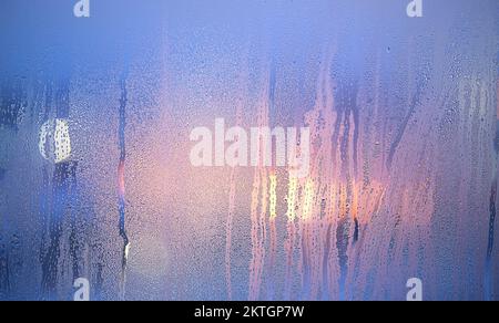 Defocused lights glowing through the misted window with drops. Stock Photo