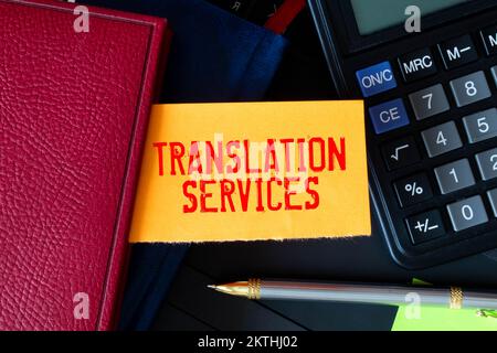 On a light background, gold-framed glasses, a flower in a pot, a green notebook, a red pen and a brown notebook with the text TRANSLATION SERVICES. Bu Stock Photo