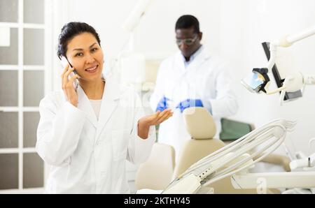 Smiling female dentist talking on mobile phone in dental office Stock Photo