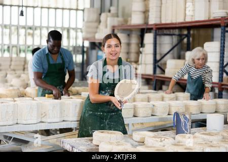 Positive young worker demonstrates half of plaster mold for pottery in pottery factory Stock Photo