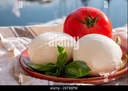 White soft italian mozzarella bufala cheese in balls with red tomato and basil served outdoor Stock Photo