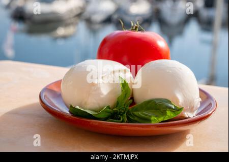 White soft italian mozzarella bufala cheese in balls with red tomato and basil served outdoor Stock Photo