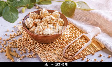 Textured soy protein chunks (nutri nuggets), raw soy meat for vegans in clay bowl on a bamboo napkin against the background of burlap and branch young Stock Photo