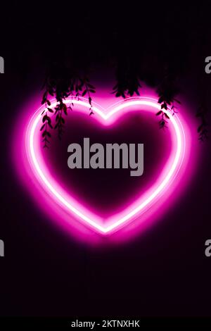 Neon pink heart on black wall with copy space Stock Photo