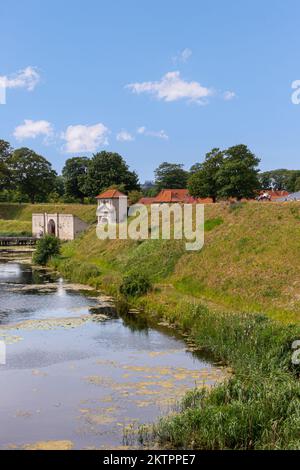 Copenhagen, Denmark - July 24, 2022: Green dirt ramparts and moat east of south entrance with bridge into historic military base Kastellet under blue Stock Photo