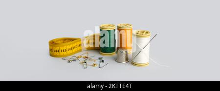 Thread spools, measuring tape, safety pins and thimble on grey background Stock Photo