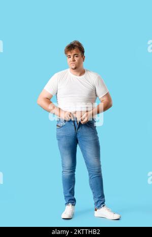 Young overweight man in tight jeans on blue background Stock Photo