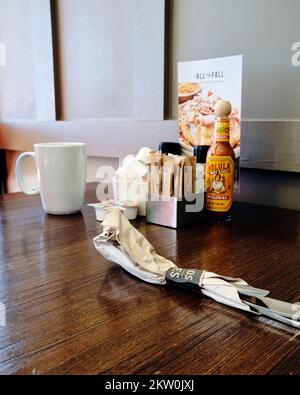 Restaurant table breakfast set up with wrapped utensils, coffee cup and condiments. Stock Photo