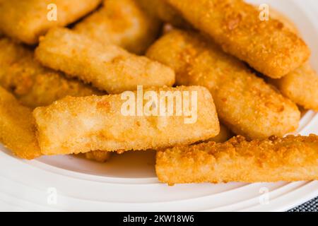 Fish sticks in a crunchy golden breading close-up on white plate on the kitchen table, selective focus Stock Photo