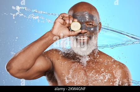 Face, water splash and senior black man with lemon and clay mask in studio isolated on a blue background. Portrait, cleaning and hygiene of elderly Stock Photo