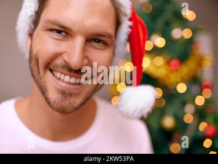 Filled with Christmas cheer. A handsome man smiling at the camera with a decorated christmas tree in the background. Stock Photo