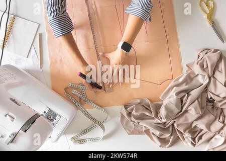 Female tailor hands draw sew pattern ruler on desk clothes creating workshop top view closeup Stock Photo