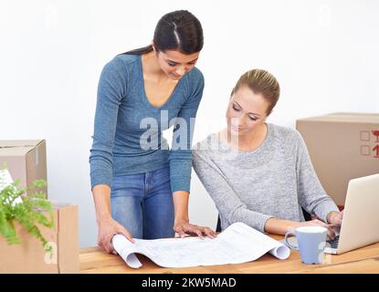 Discussing the designs their new space. two young female entrepreneurs looking at blueprints in their new office. Stock Photo