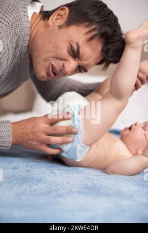 Changing diapers is an awful job. A young father making a face as he smells his babyamp039s diaper. Stock Photo