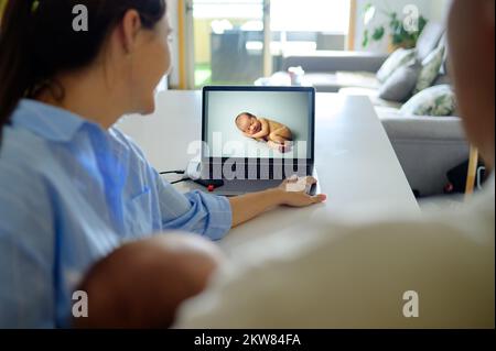 Crop family watching photos of newborn on computer with memory drive Stock Photo