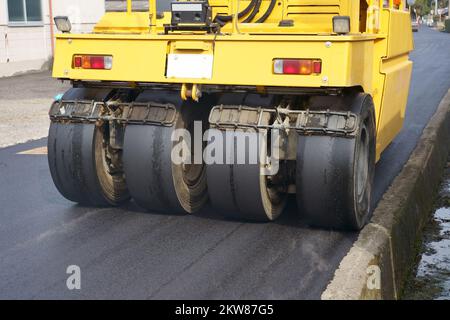 Pneumatic roller of tires compacting new asphalt of a street. Repaving the road surface. Road works. Stock Photo