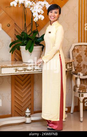 Vietnamese hotel receptionist posing for portrait wearing ao dai, Ho Chi Minh City, Vietnam Stock Photo